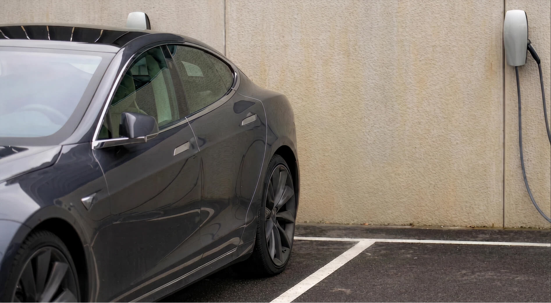 Gray Tesla Model 3 parked at a wall-mounted EV charging station